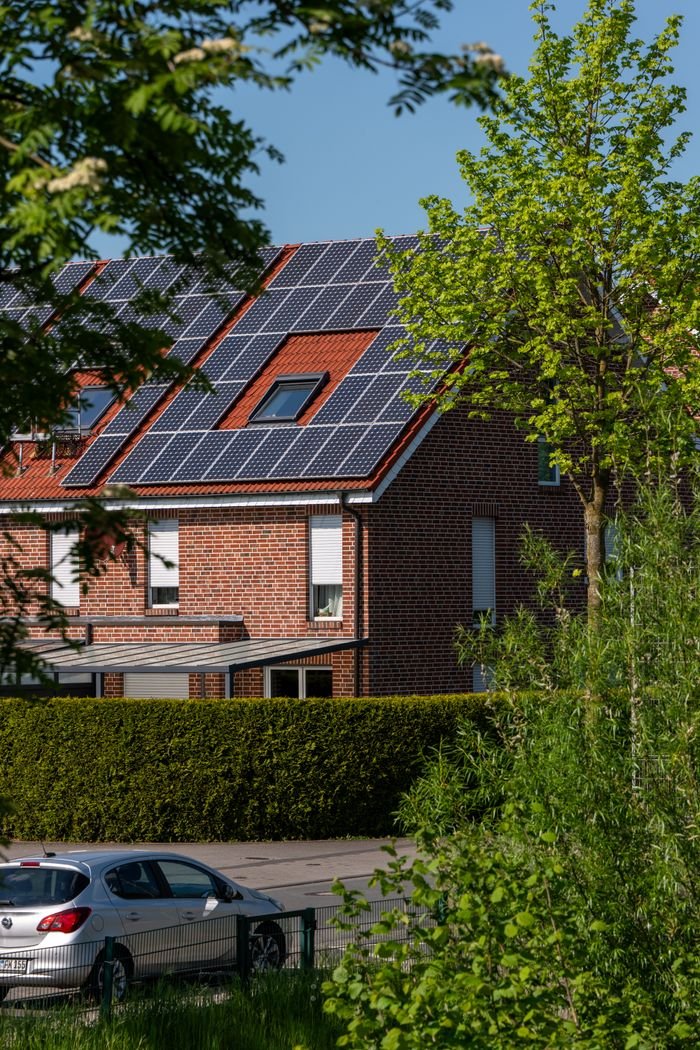 Services A modern brick house with solar panels on the roof, surrounded by lush greenery, under a clear blue sky.